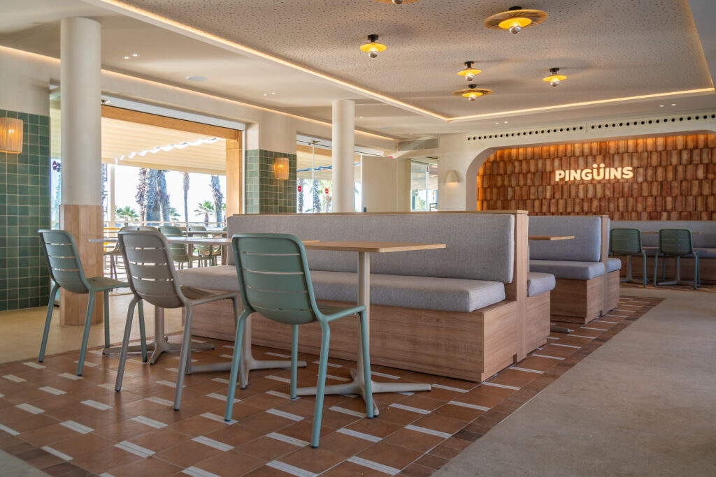 Interior de Pingüins con bancos verdes, mesas de madera y el logotipo iluminado al fondo